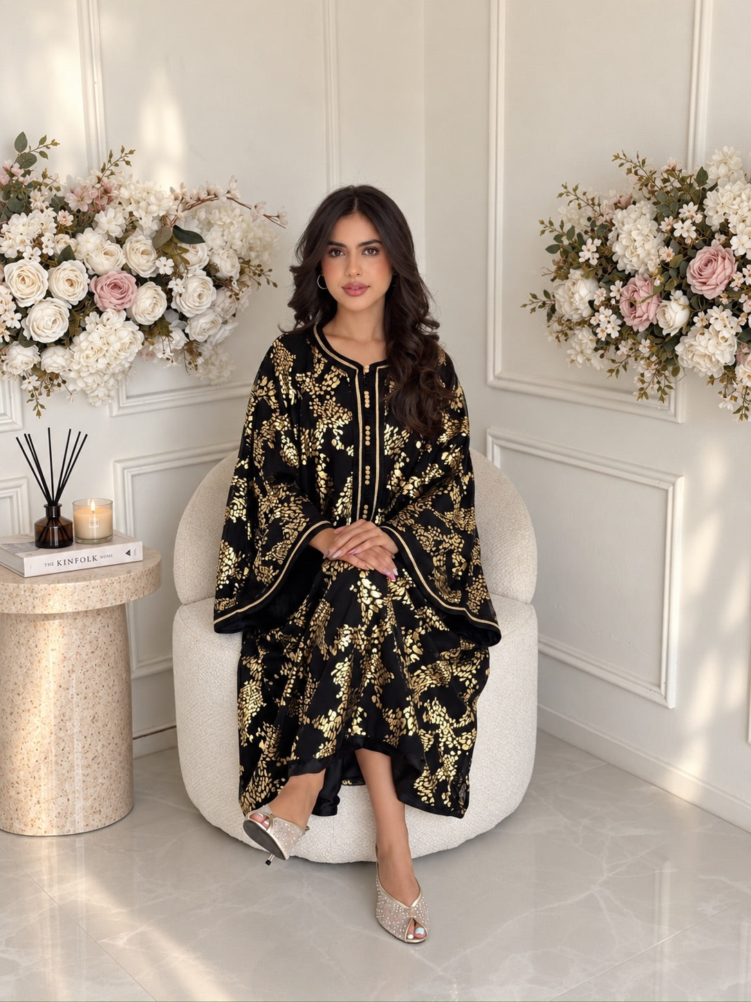 Full-length seated view of Gandoura Raya, a black and gold Moroccan dress with a flowing silhouette