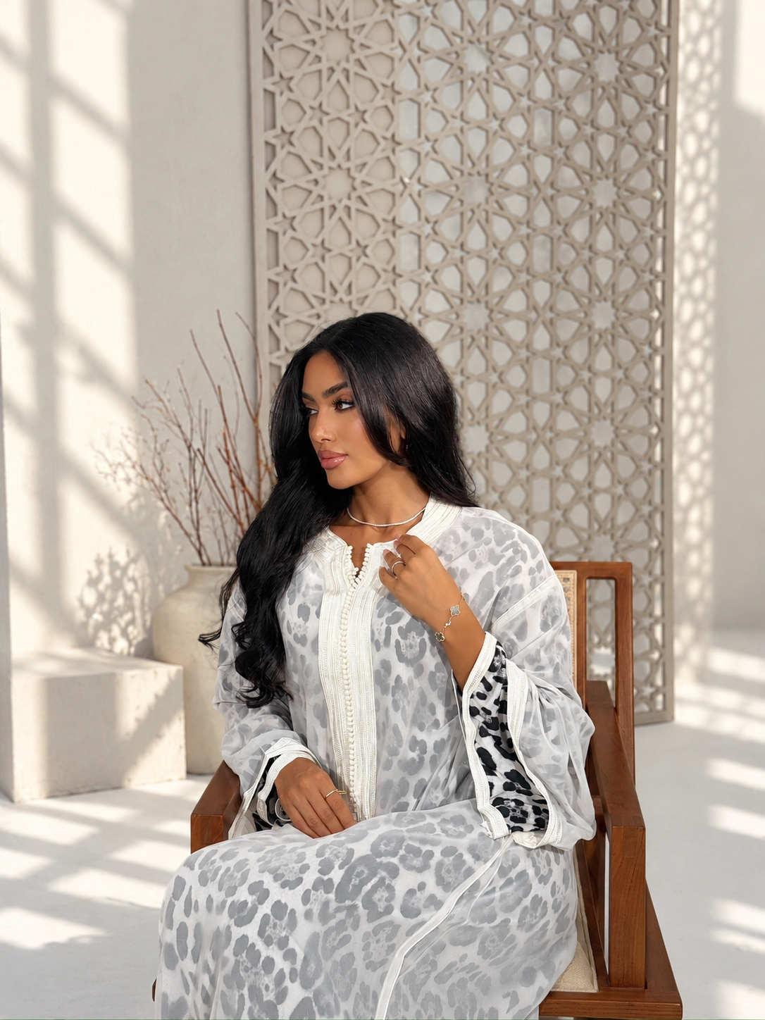 Model seated in Reine leopard print Moroccan caftan, showing the wide sleeves and decorative cuffs