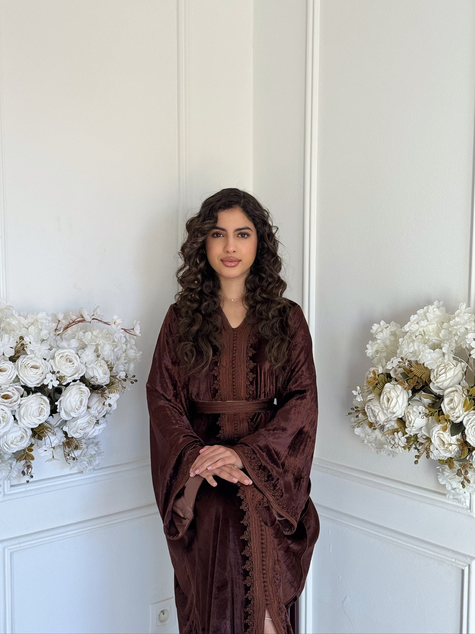 Brown velvet Moroccan caftan with refined embroidery displayed in an elegant interior with white floral decor