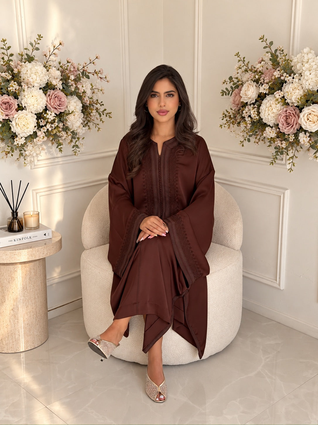 Full-length seated view of Gandoura Ritaj, a brown Moroccan dress with wide sleeves