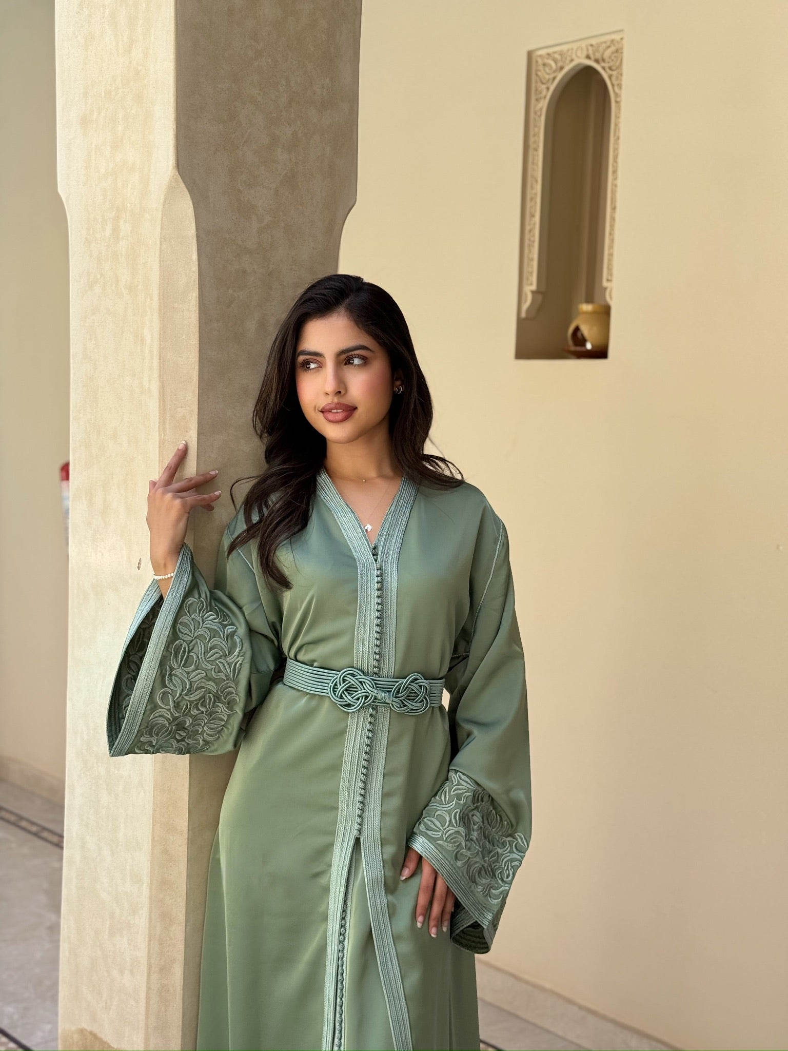 Woman wearing a sage green takchita with a defined waist and embroidered sleeve detailing