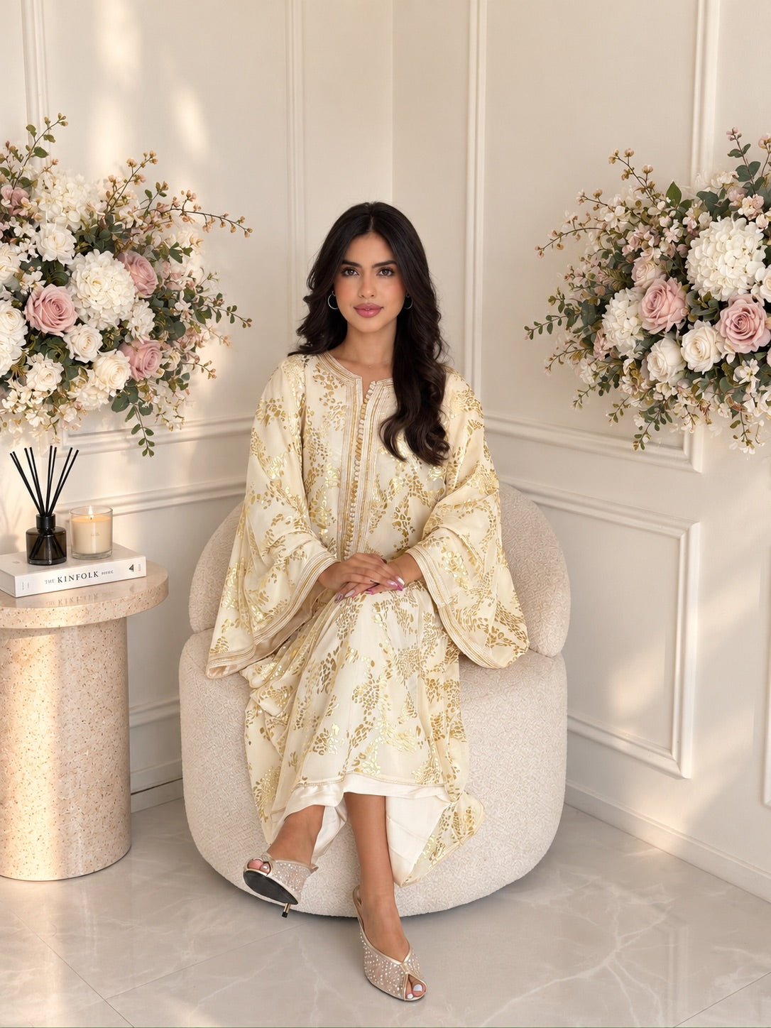 Model seated in ivory Gandoura Ameera with a gold-toned floral pattern and wide sleeves