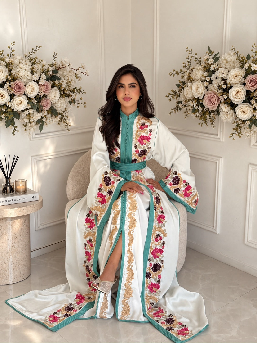 Full-length seated view of Takchita Lamis, a two-piece ivory Moroccan dress with floral embroidery and turquoise trim