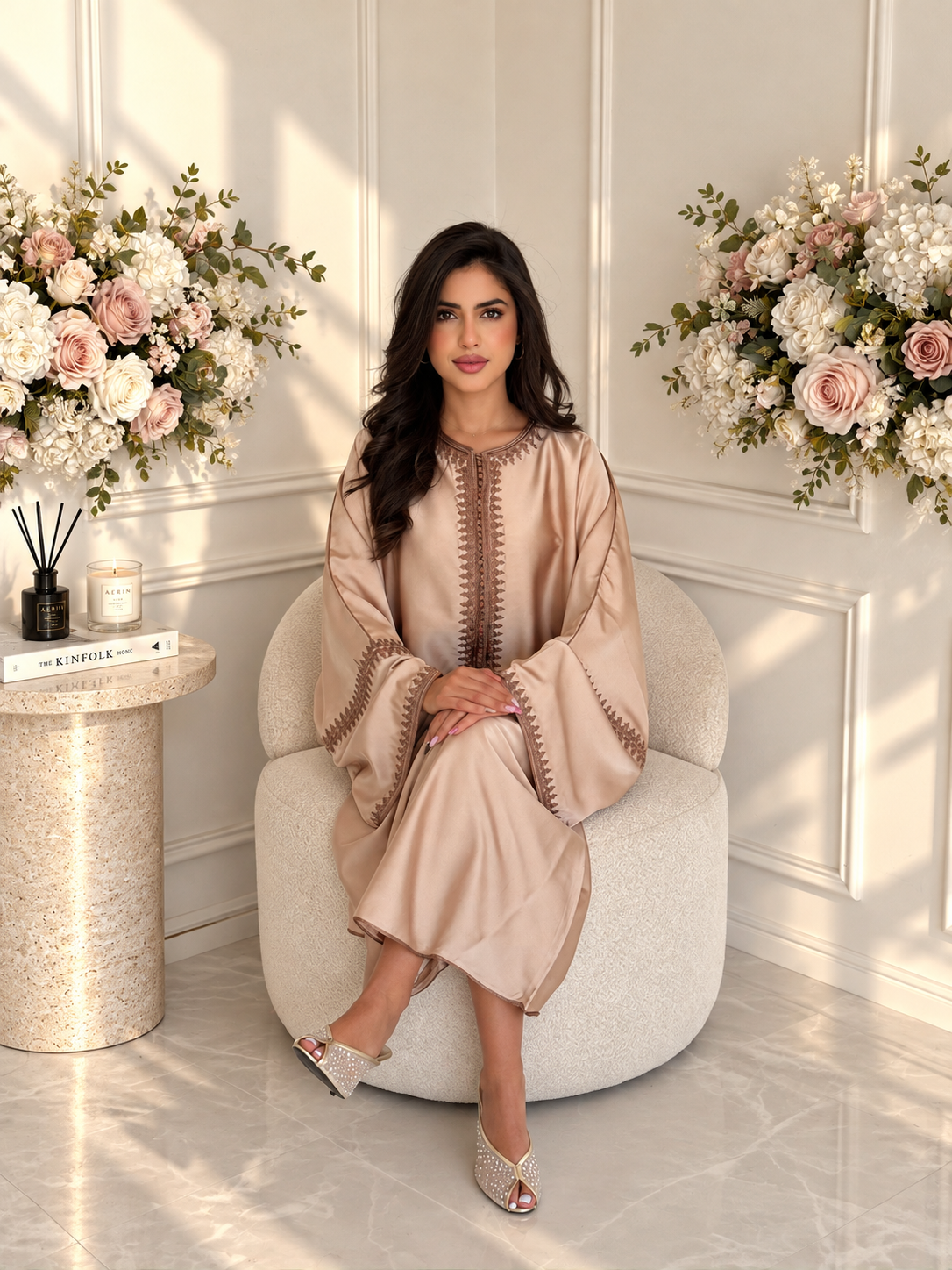 Full-length seated view of champagne Moroccan Gandoura Zaynab with wide sleeves and brown embroidered trim